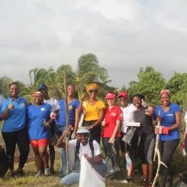 A group of volunteers in matching blue and red T-shirts and caps stands together outdoors under palm trees.