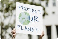 Hands holding up a hand-painted sign reading "Protect our planet"